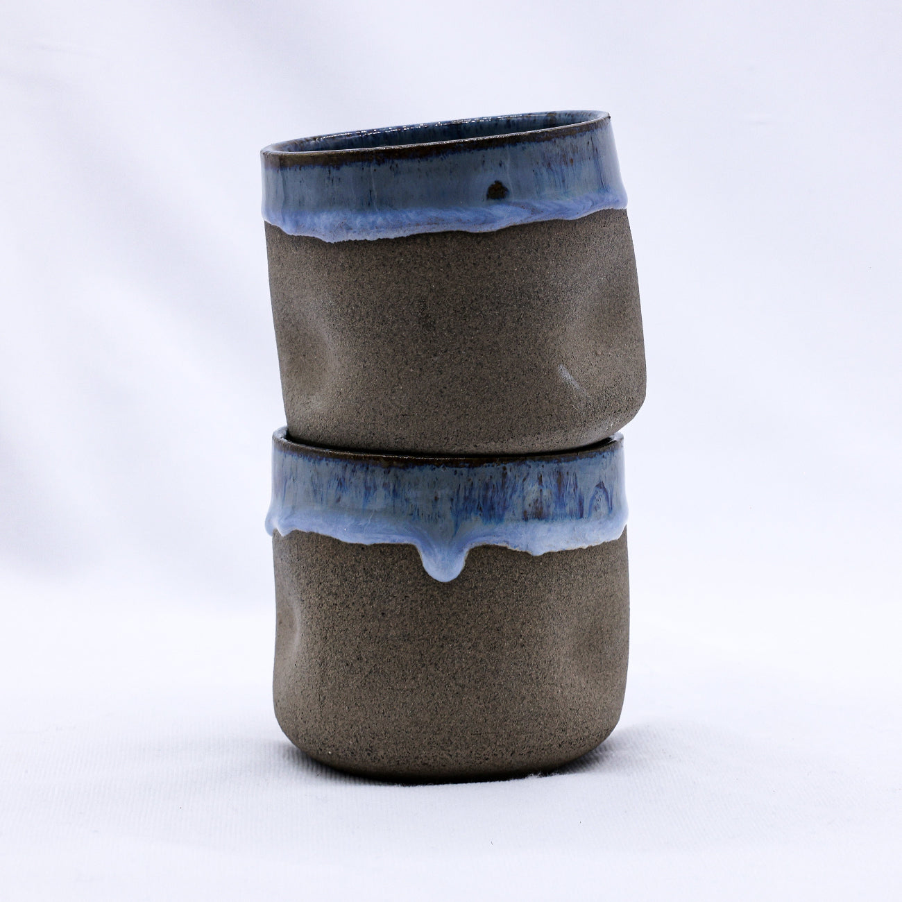 Two stacked ceramic tumblers with blue rim on a white background