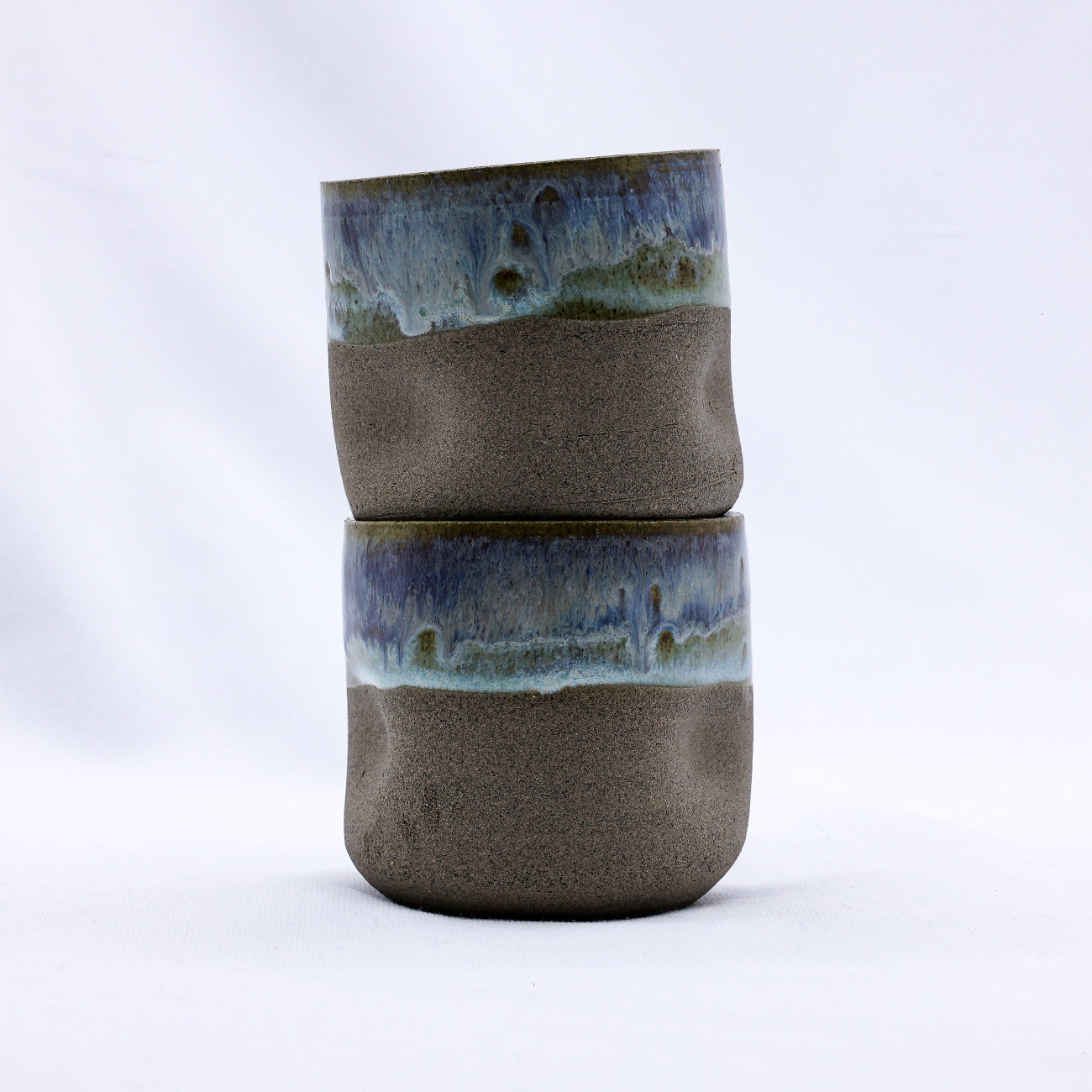 Stack of two ceramic cups with layered glaze on a white background