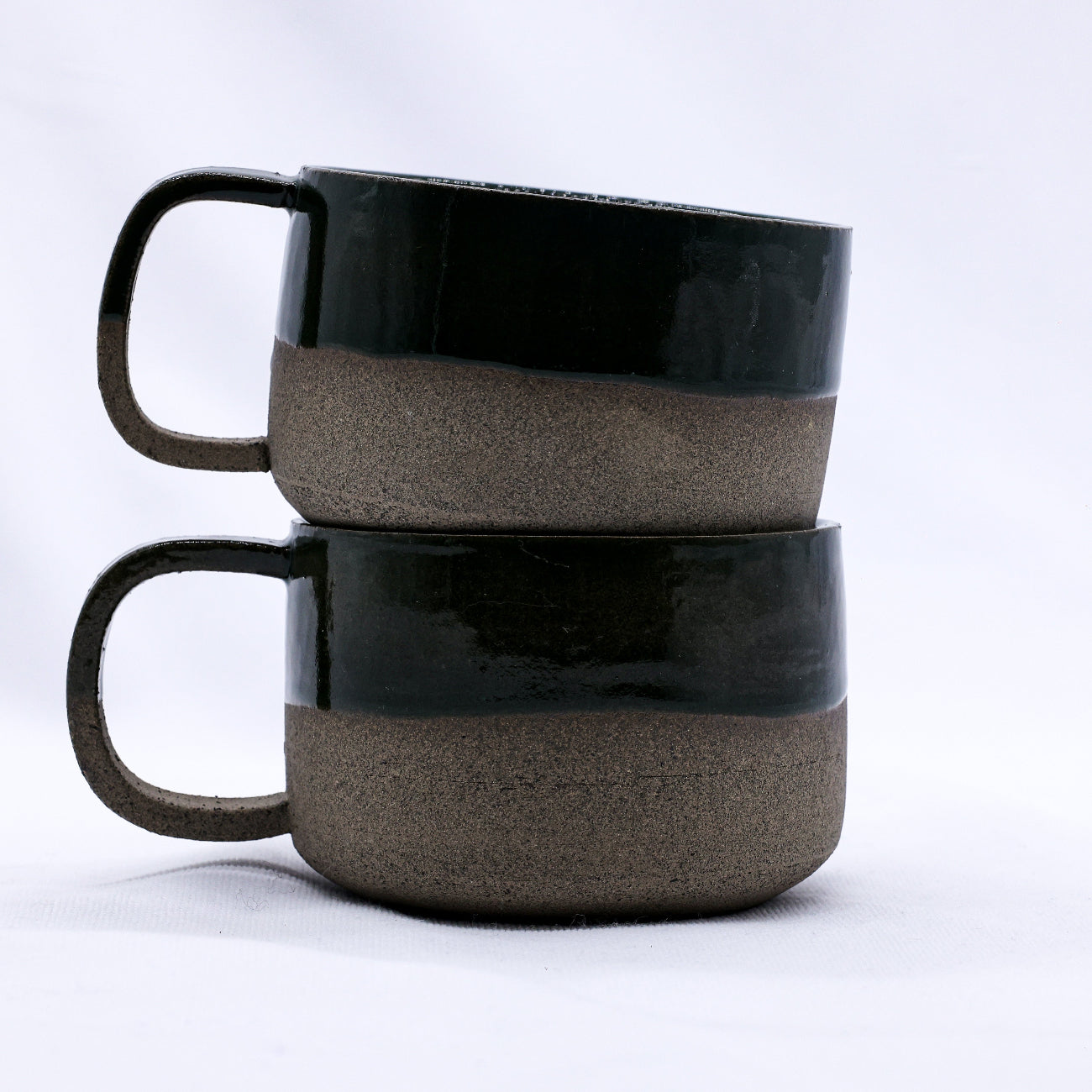 Two stacked ceramic mugs with black and brown gradient on a white background