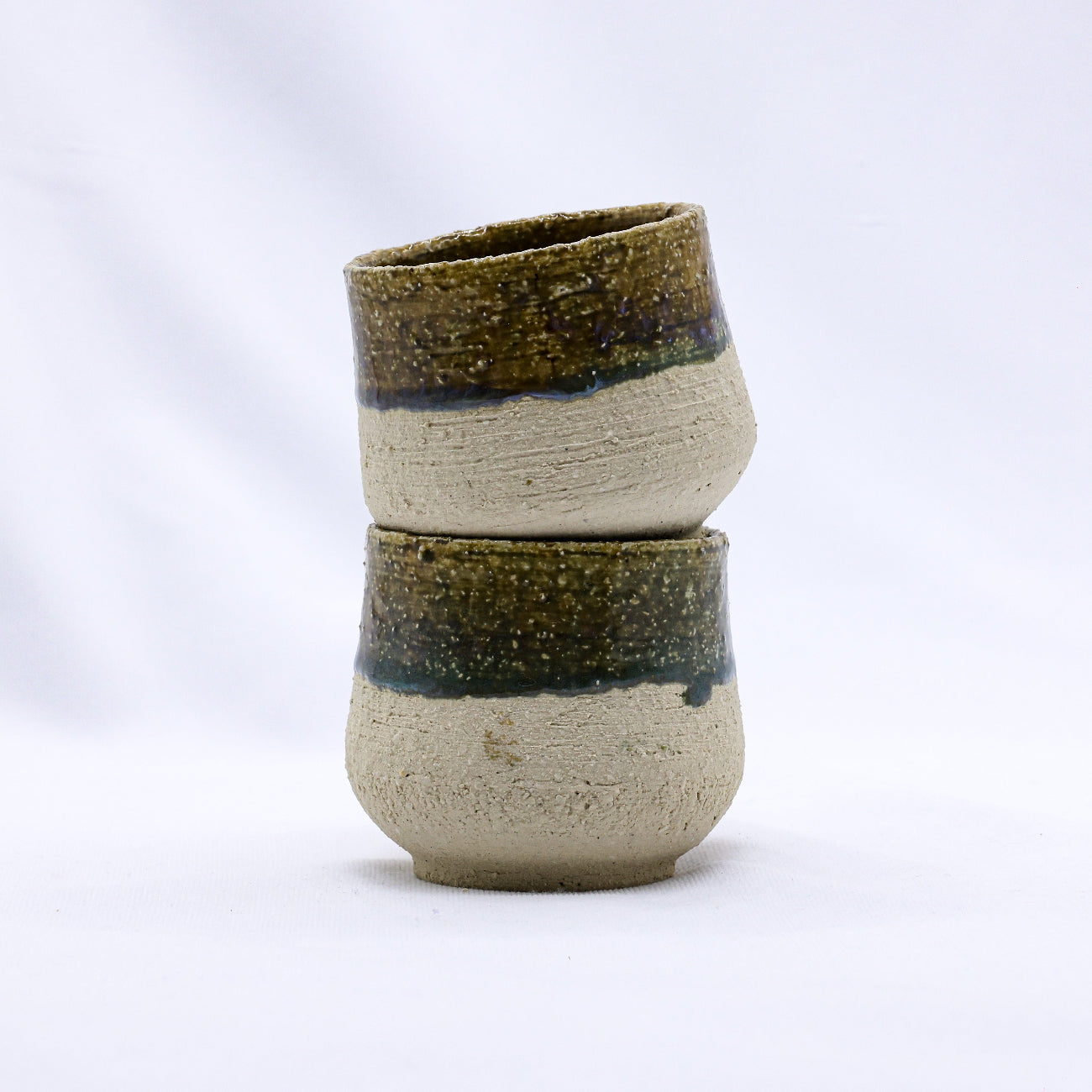 Two stacked ceramic cups with green and beige design on a white background