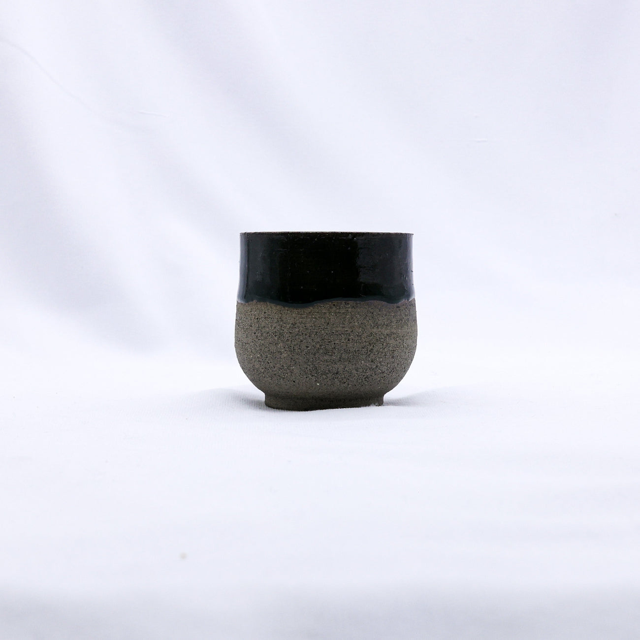 Ceramic cup with black top and textured gray bottom on a white background