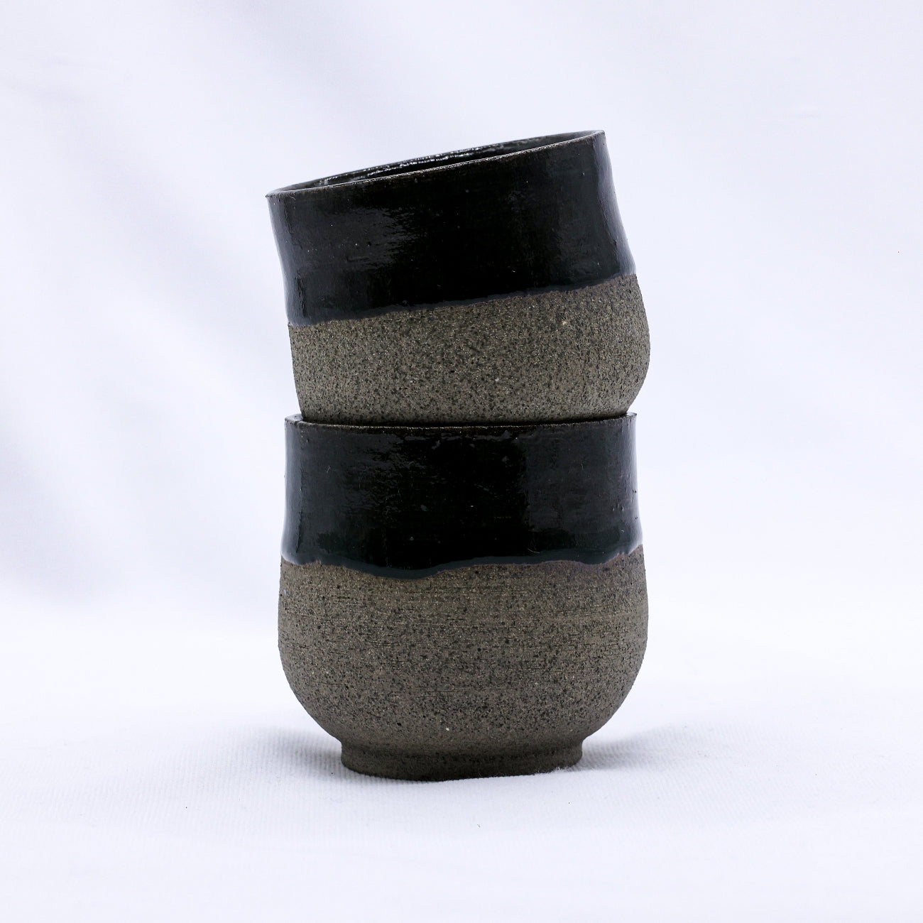 Two stacked ceramic cups with black and gray speckled design on a white background