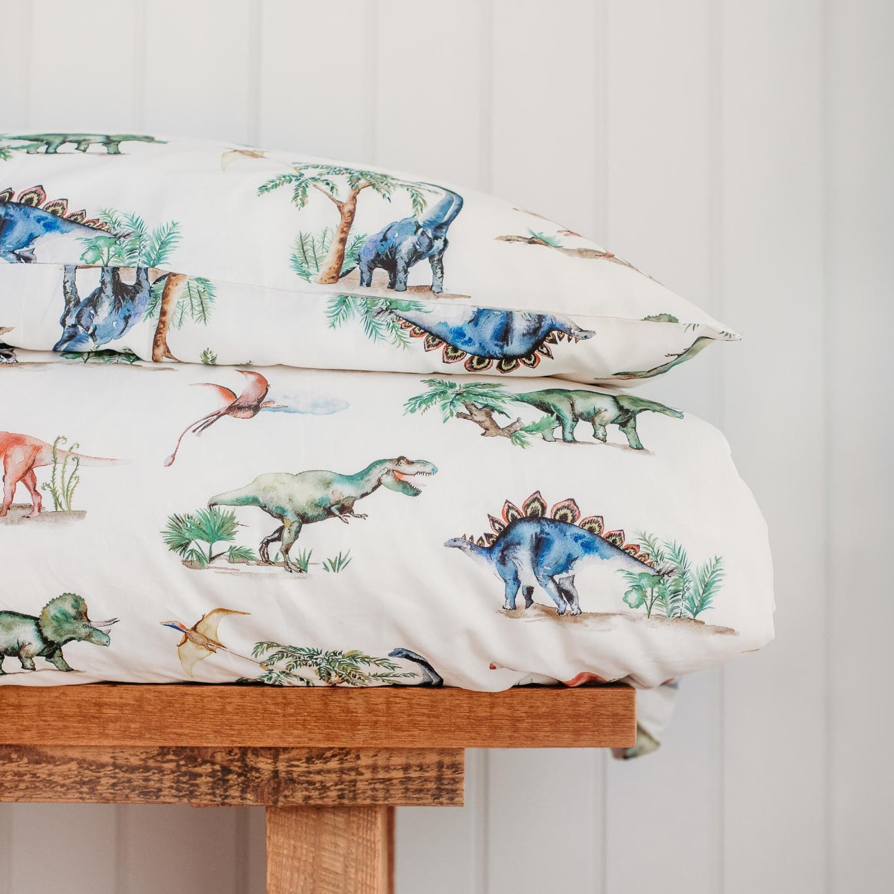 Dinosaur-themed pillowcases on a wooden surface with a light gray background