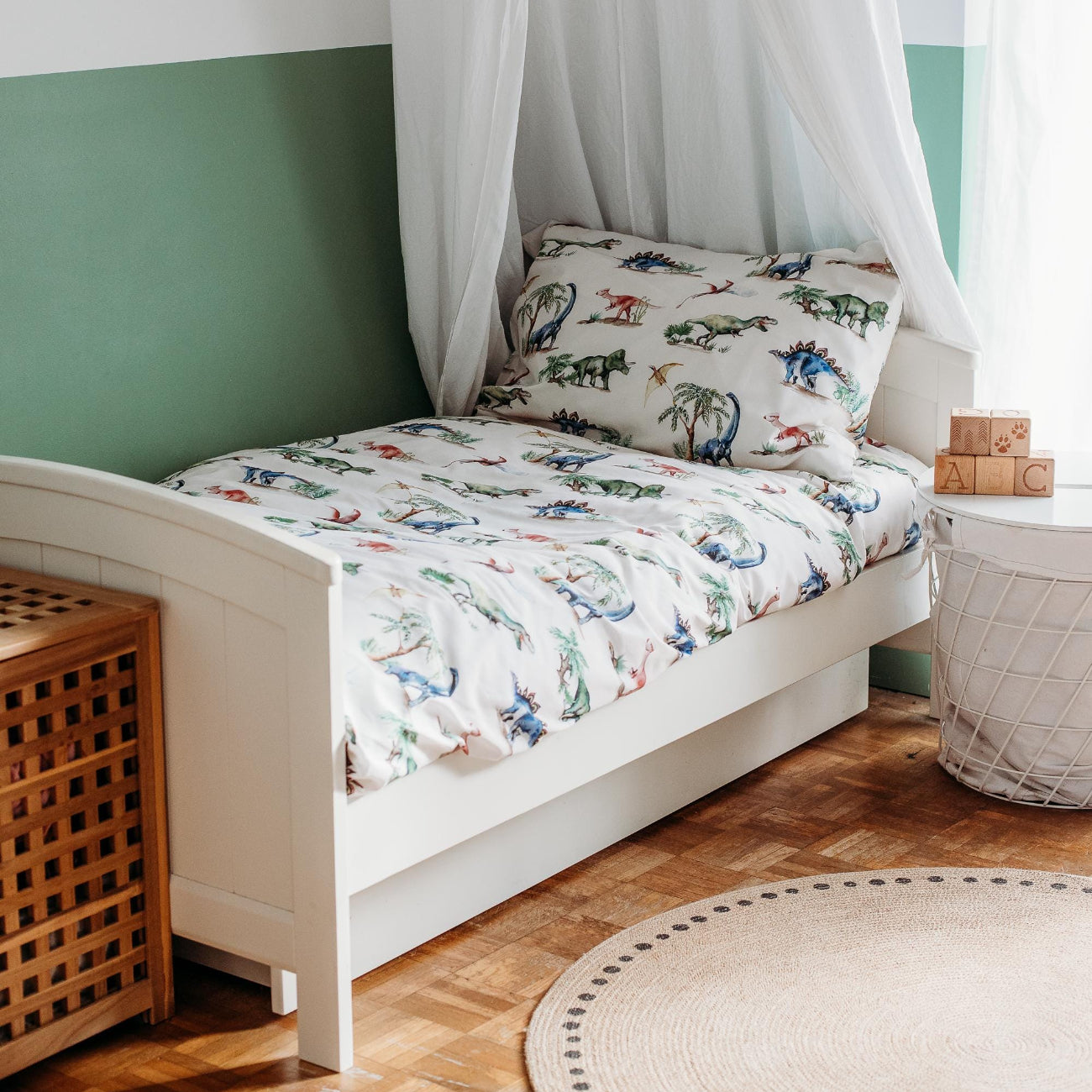 Children's bedroom with a white canopy bed featuring dinosaur-themed bedding and pillows.