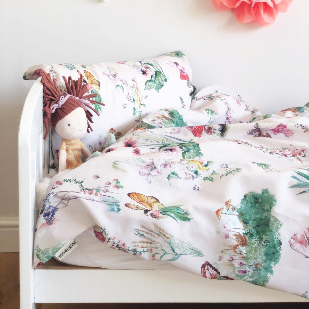 Floral-patterned comforter on a bed with a stuffed animal, against a light wall with flowers.