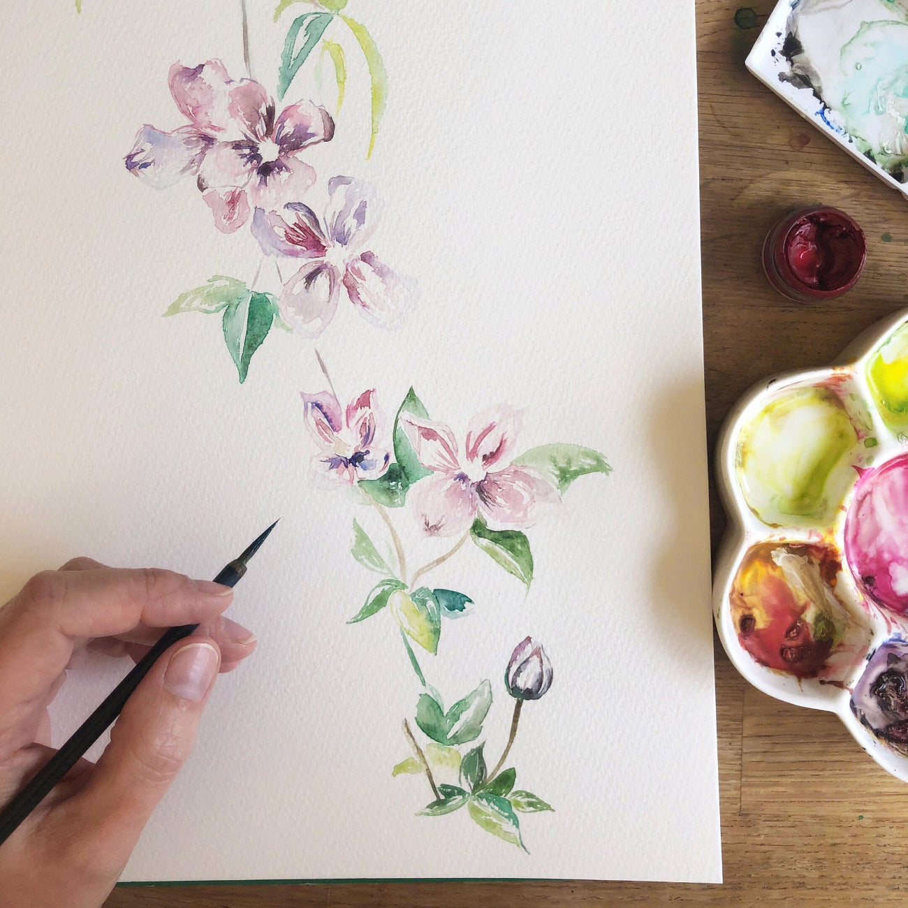 Hand painting a floral design on paper with watercolour paints.