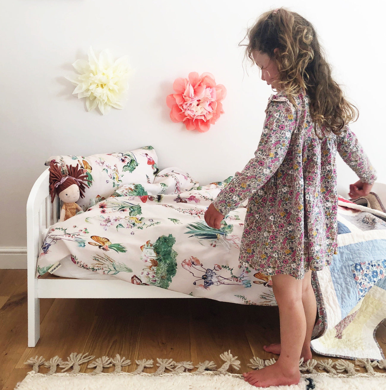 Child in a floral dress standing next to a bed with colourful bedding in a room with decorative flowers on the wall.