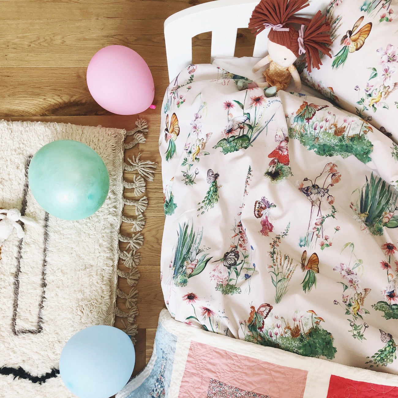 Floral-patterned bedspread on a bed with colourful balloons on a wooden floor.