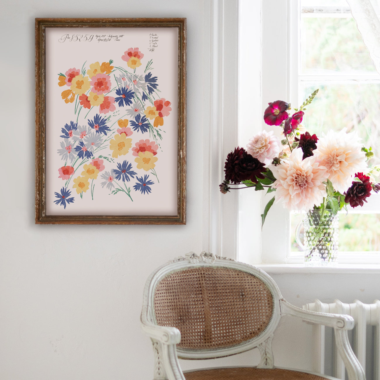 Floral artwork on a wall next to a chair with a window displaying flowers in the background