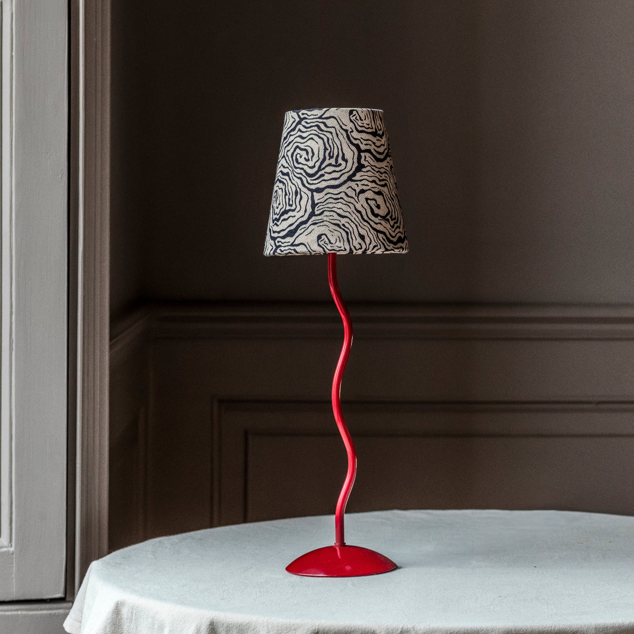 Table lamp with a red base and black and white patterned shade on a round table.