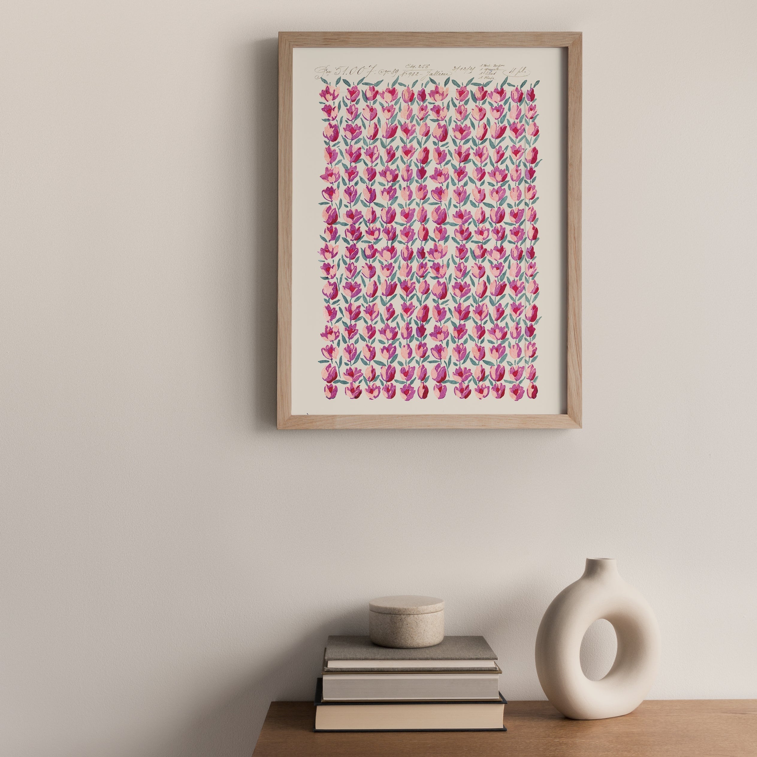 Framed artwork with pink tulip pattern on a wall above a wooden cabinet with decorative items.