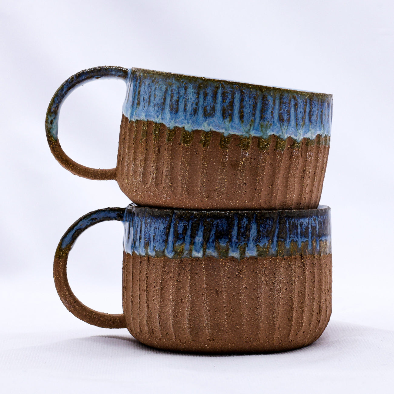 Two brown ceramic mugs with blue rims stacked on a white background