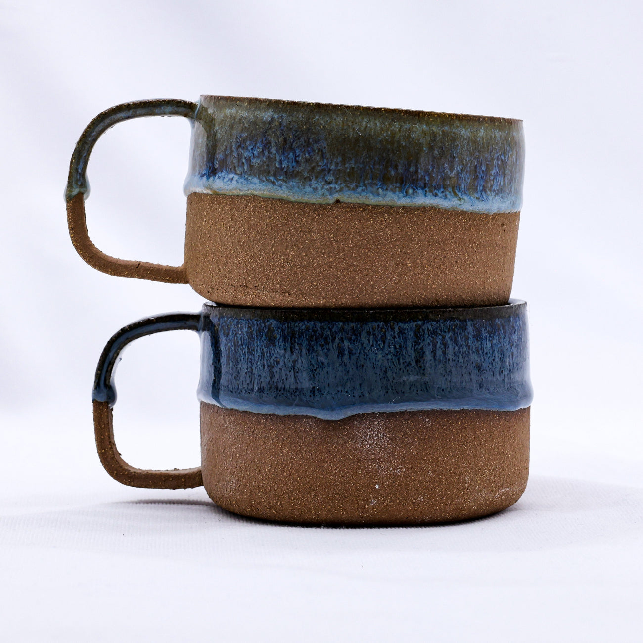 Two ceramic mugs with blue rim and brown body on a white background