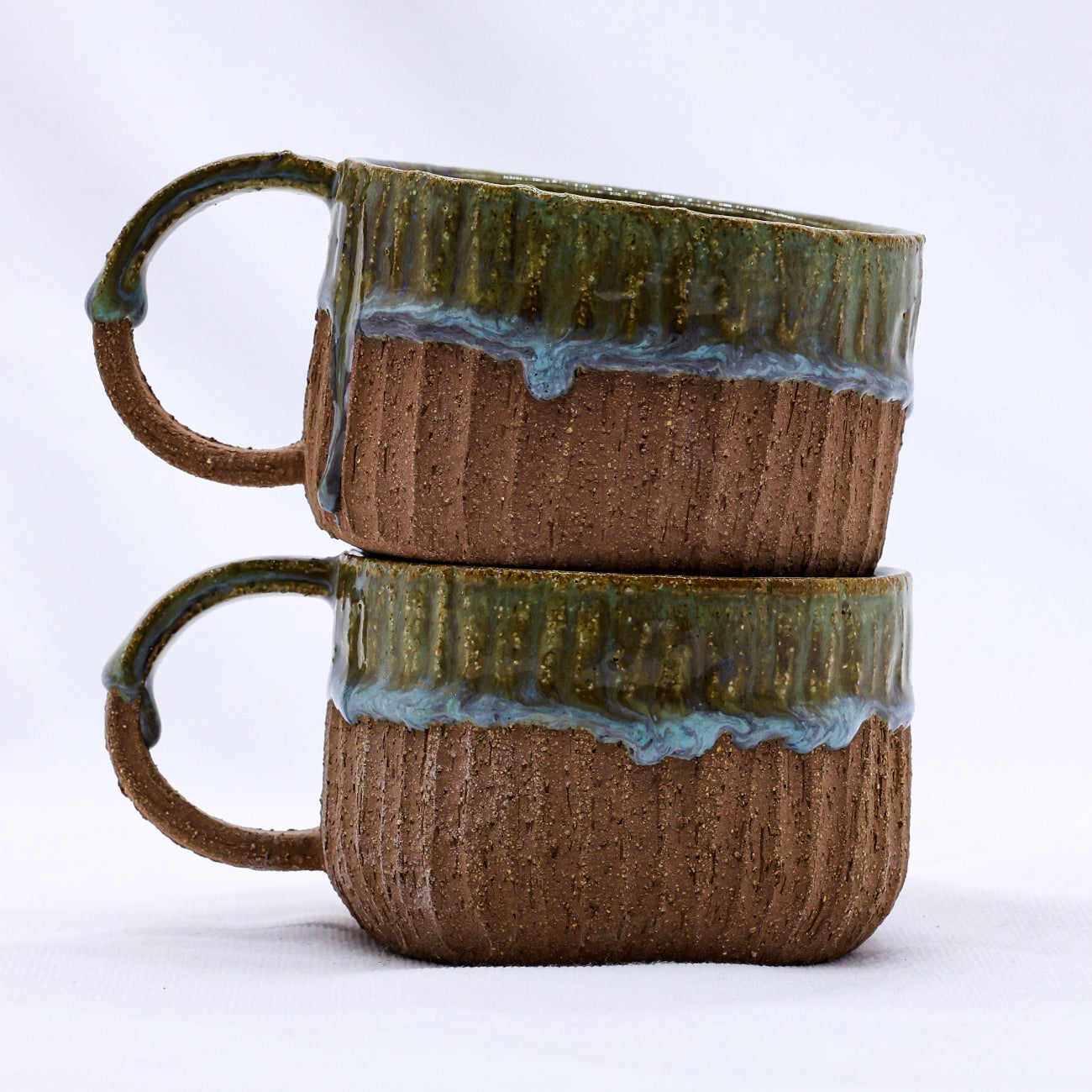 Two stacked ceramic mugs with green and brown glaze on a white background