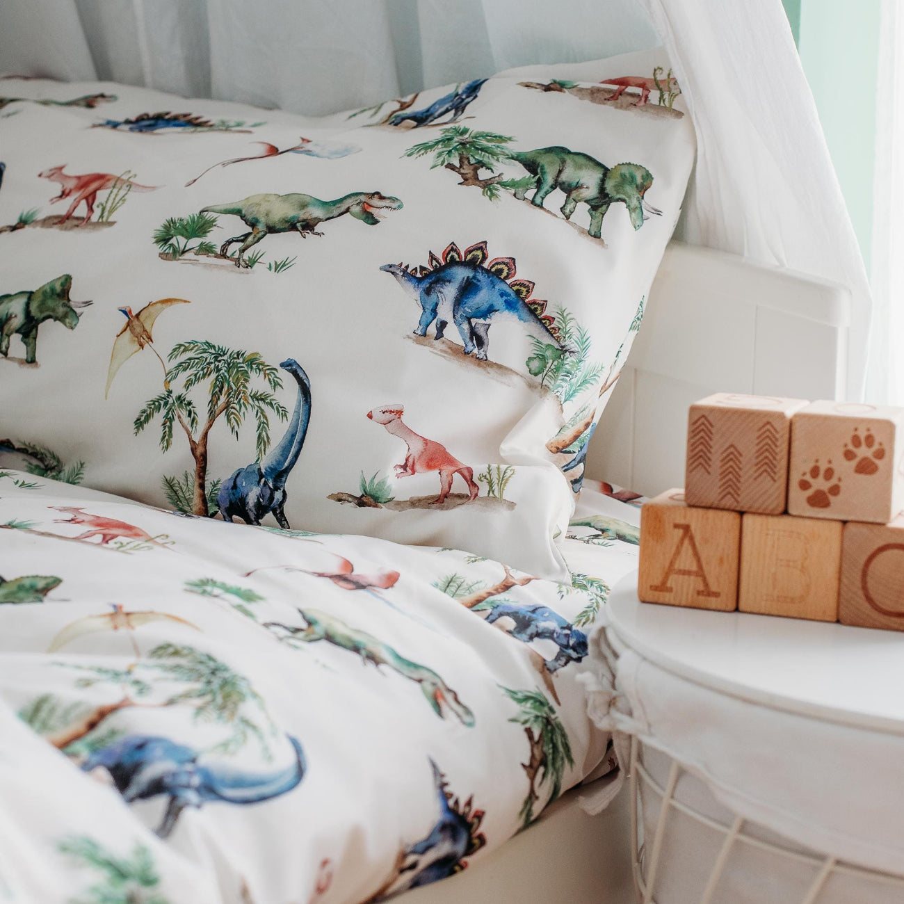 Children's bed with dinosaur-themed bedding and wooden blocks on a nightstand.