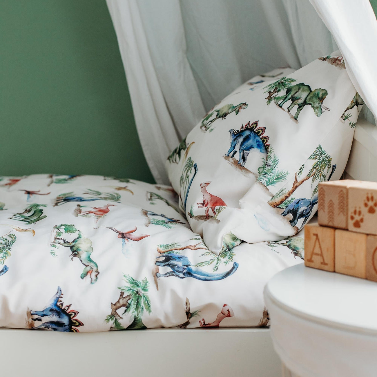 Children's room with dinosaur-themed bedding and blocks on a green wall.