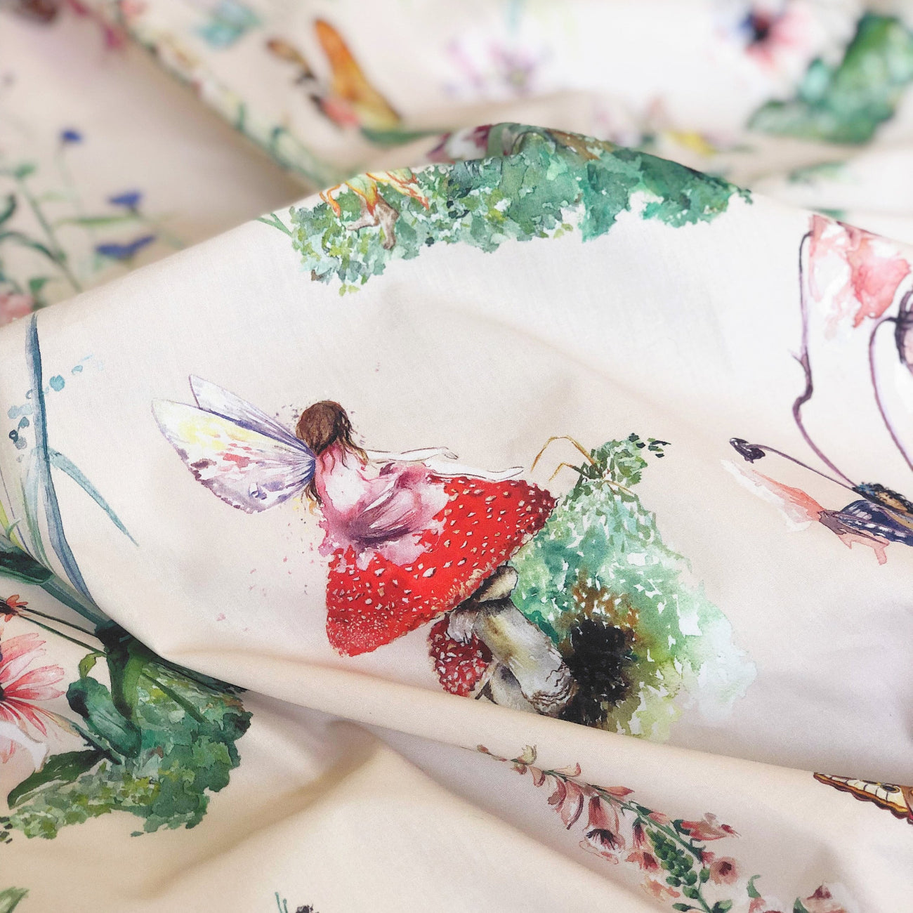 Fabric with fairy and floral design, featuring a red mushroom and greenery.