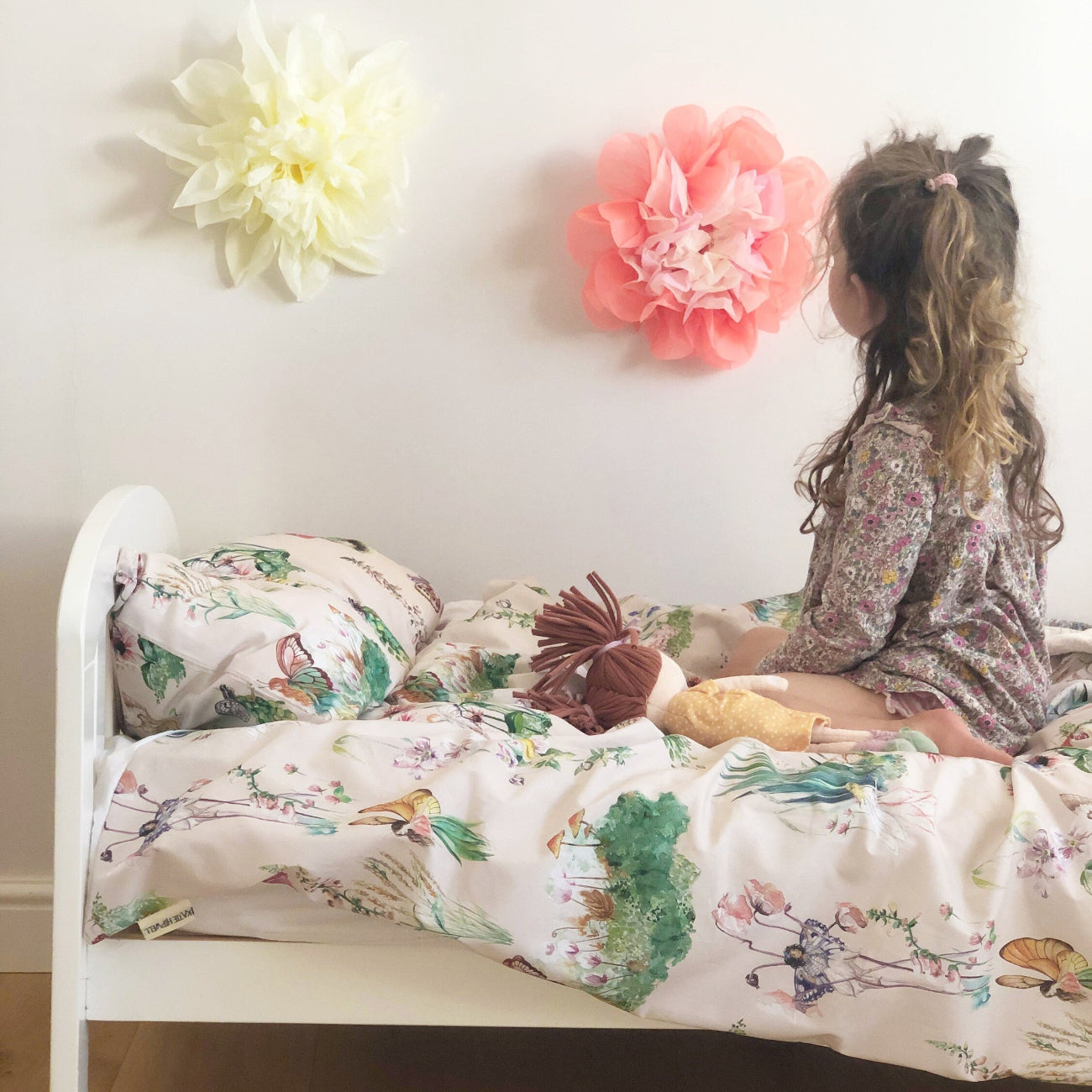 Child sitting on a bed with floral bedding in a room with decorative flowers on the wall.