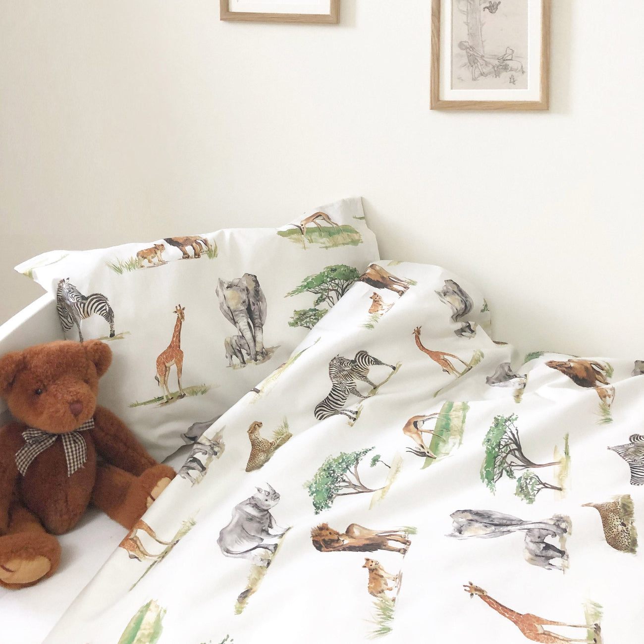 Children's room with animal-patterned bedding and pillows, teddy bear, and framed artwork on the wall.