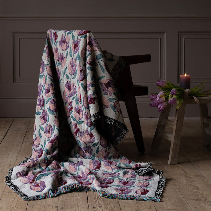 Tulip patterned blanket draped over a wooden chair against a dark wall.